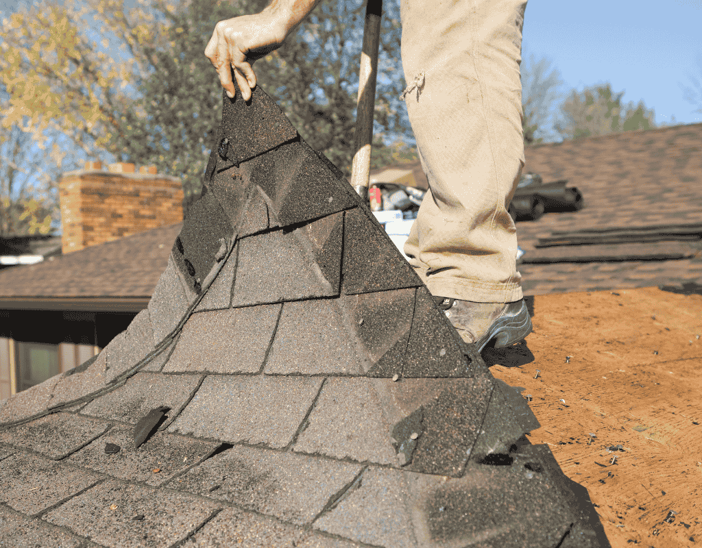 Roofer removing old asphalt shingles during residential roof replacement project