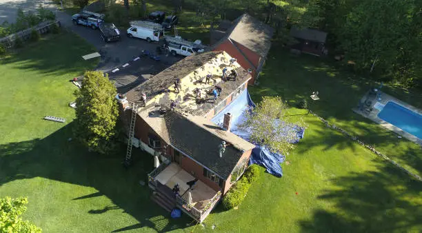 Experienced roofer tracing active leak path beneath damaged shingles and flashing